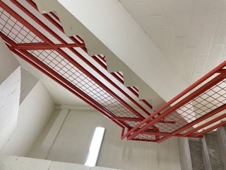 Red steel stair guardrail with mesh infill in a stairwell